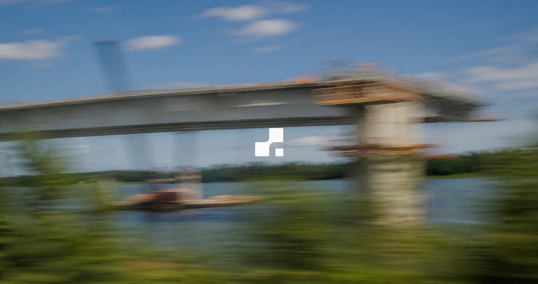 Vue estivale floutée par le mouvement d’un pont en construction au-dessus d’une rivière, sur laquelle figure le symbole Aplon